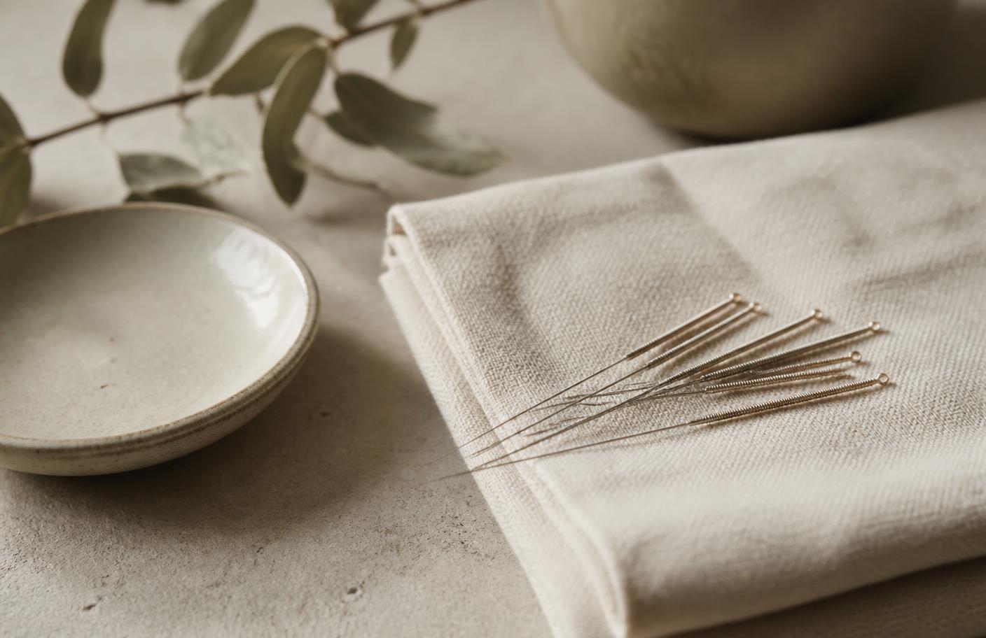 Fine acupuncture needles resting on folded pale linen in soft daylight.